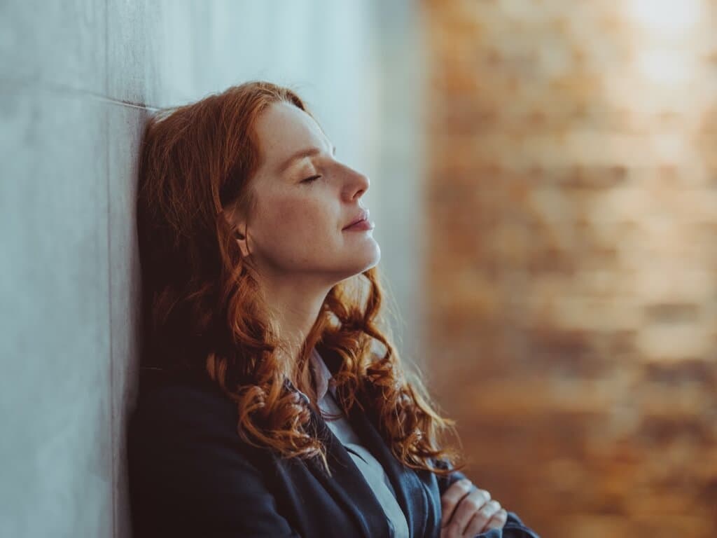 Naine suleb silmad ja toetub seinale, tema poos peegeldab mõtisklevat ja rahulikku meeleolu